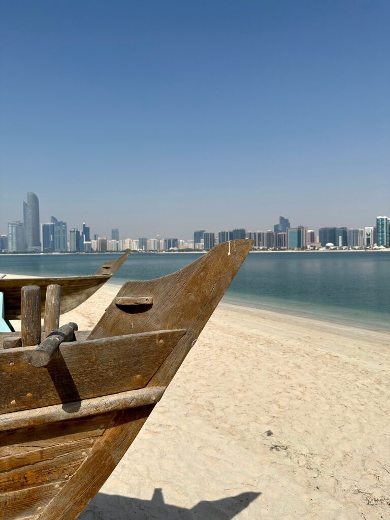 Traditional wooden dhow boat on a sandy beach with the modern city skyline in the background, representing the wide coverage of storage services Abu Dhabi.