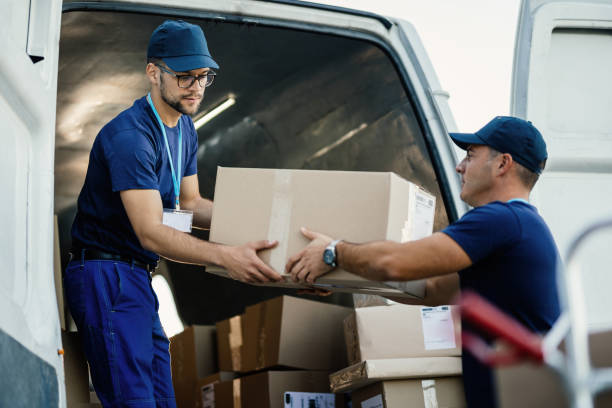 Professional team members in blue uniforms loading cardboard boxes carefully into a moving van, demonstrating reliable services from movers and packers MBZ City.