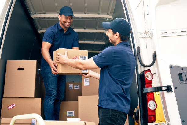 Two professional office movers Abu Dhabi team members passing a cardboard box out of a moving truck during a business relocation.