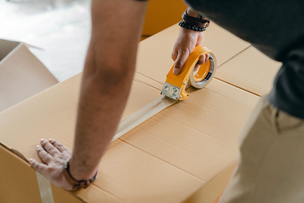 Close-up of a mover using a yellow tape dispenser to securely seal a large cardboard box, demonstrating professional services by Abu Dhabi movers and packers.
