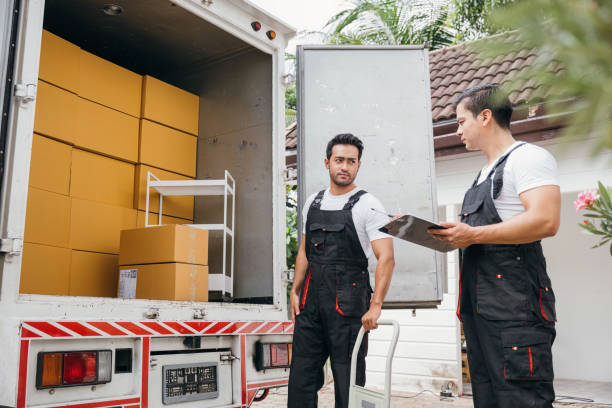 Two professional relocators in dark dungarees checking a clipboard next to a delivery truck filled with cardboard boxes, demonstrating reliable services from movers and packers Mussafah.