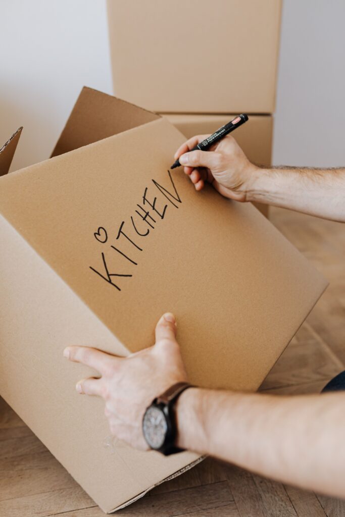 Writing "KITCHEN" on a cardboard box using a black marker to prepare items for climate-controlled storage services Abu Dhabi.