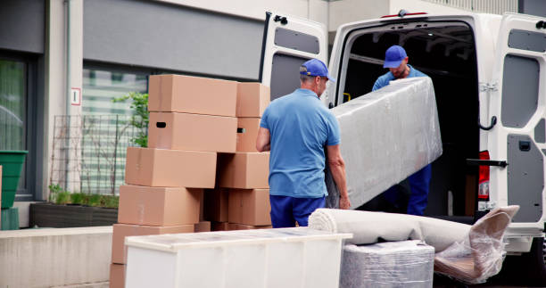 Two movers loading wrapped mattress and furniture into the back of a moving van.
