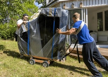 Specialized movers carefully transporting a wrapped piano on a heavy-duty dolly during a home relocation in Abu Dhabi.