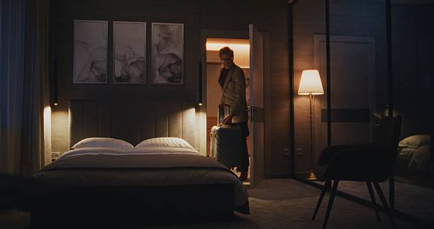 Man rolling suitcase into a modern hotel bedroom while conducting a room audit.