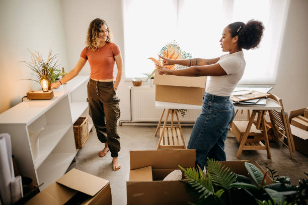 Two women unpacking moving boxes and decorating a studio apartment room together in Abu Dhabi.