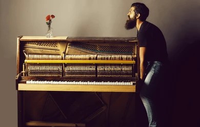 : Man straining while trying to lift a heavy upright piano without assistance.