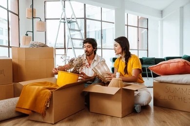 Couple packing household items and decor into labeled cardboard moving boxes.