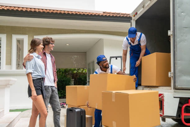 Professional movers loading cardboard boxes into a moving truck outside a villa.