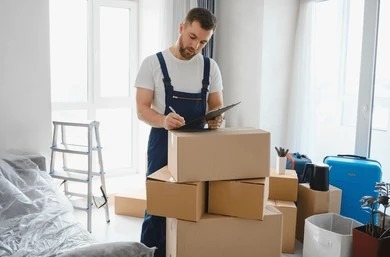 Professional mover writing on checklist clipboard leaning on cardboard moving box.